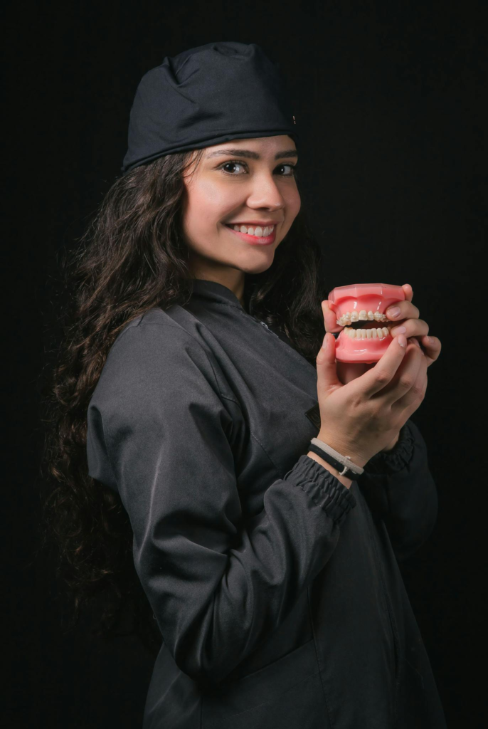 Smiling young female dentist with curly hair holding a dental model in a studio.